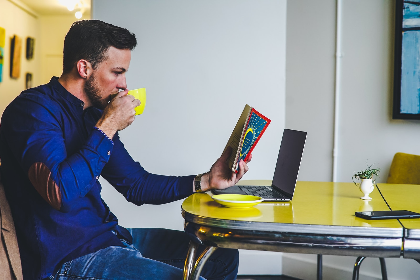 man drinking coffee in kitchen, reading book