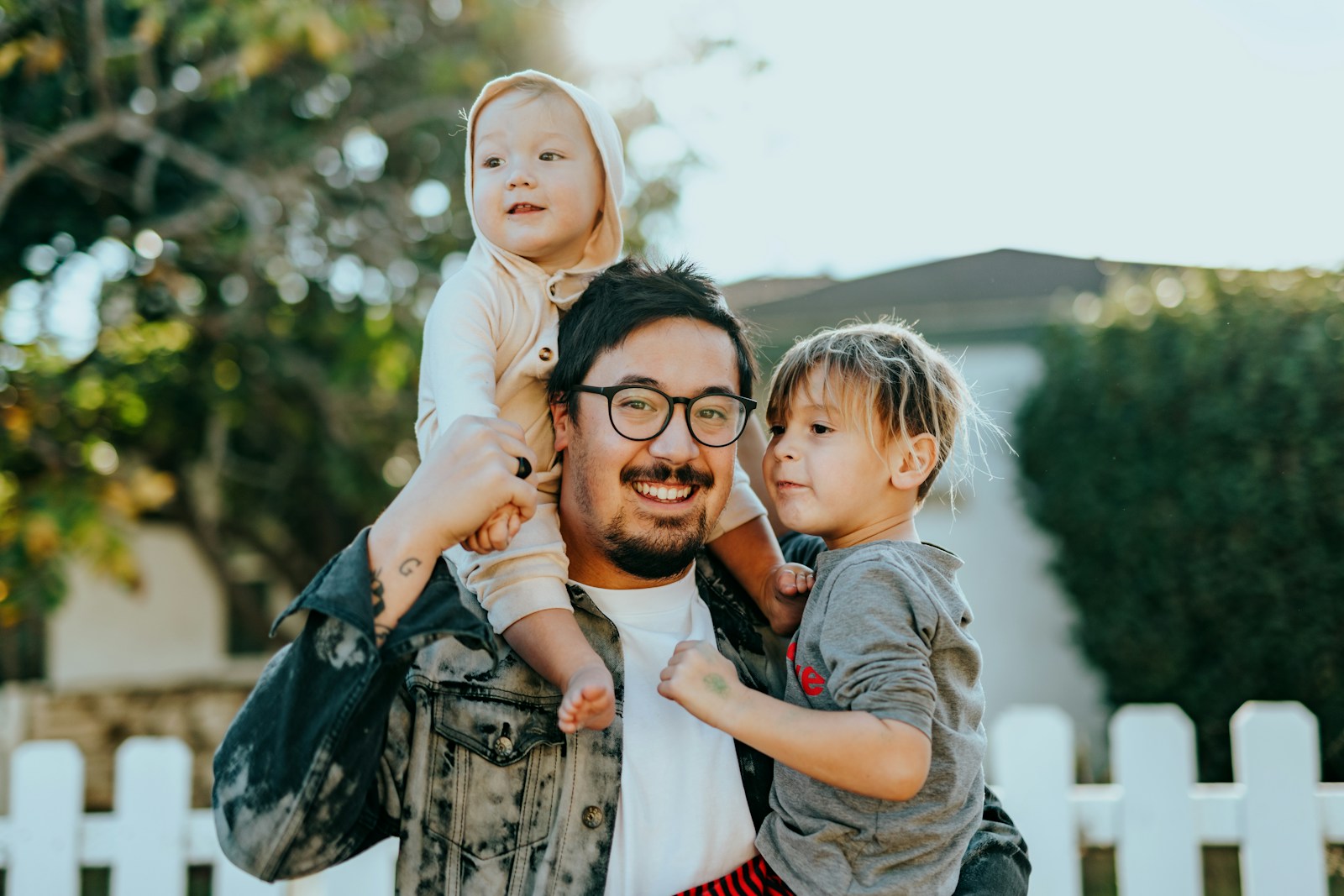 man in white shirt carrying child in gray shirt with toddler on his shoulders